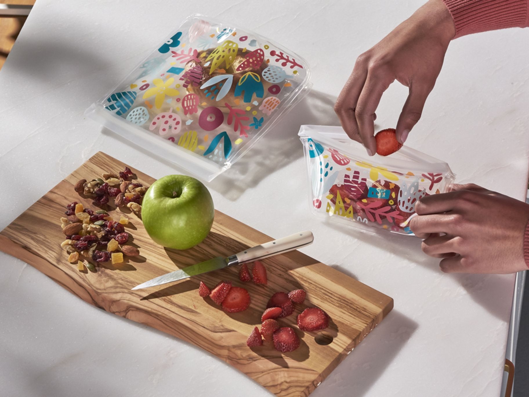 a pair of hands placing strawberries and nuts into reusable plastic food storage bags