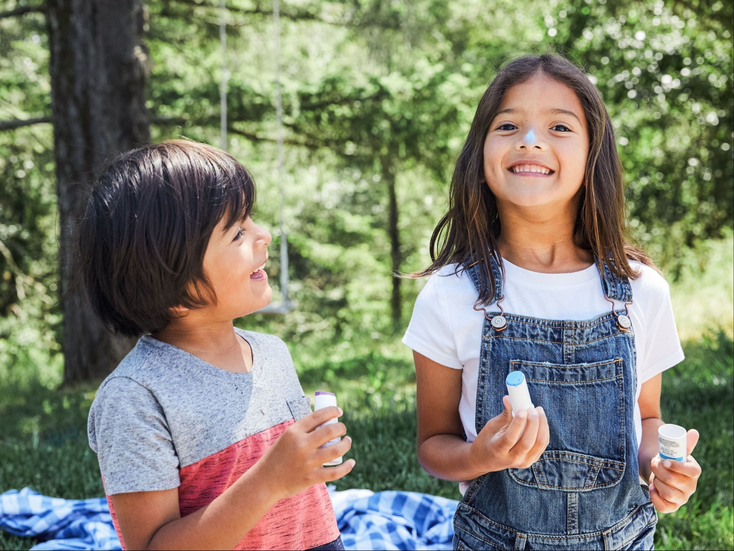 young boy and young girl putting on natural sunscreen outside in the woods