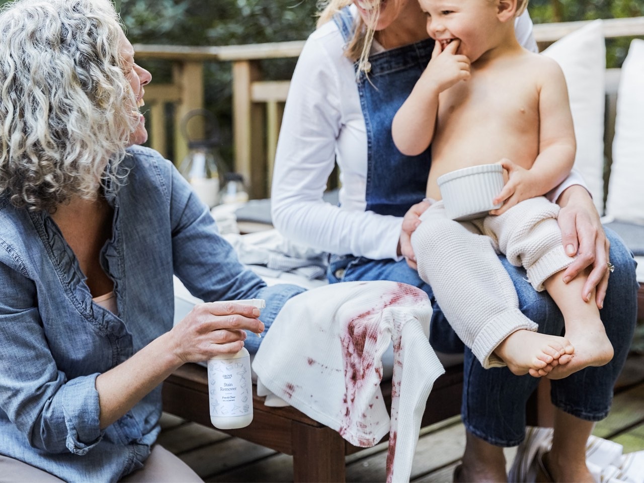 Image of older woman using Grove Stain Remover Spray on a stained white shirt looking at a young child