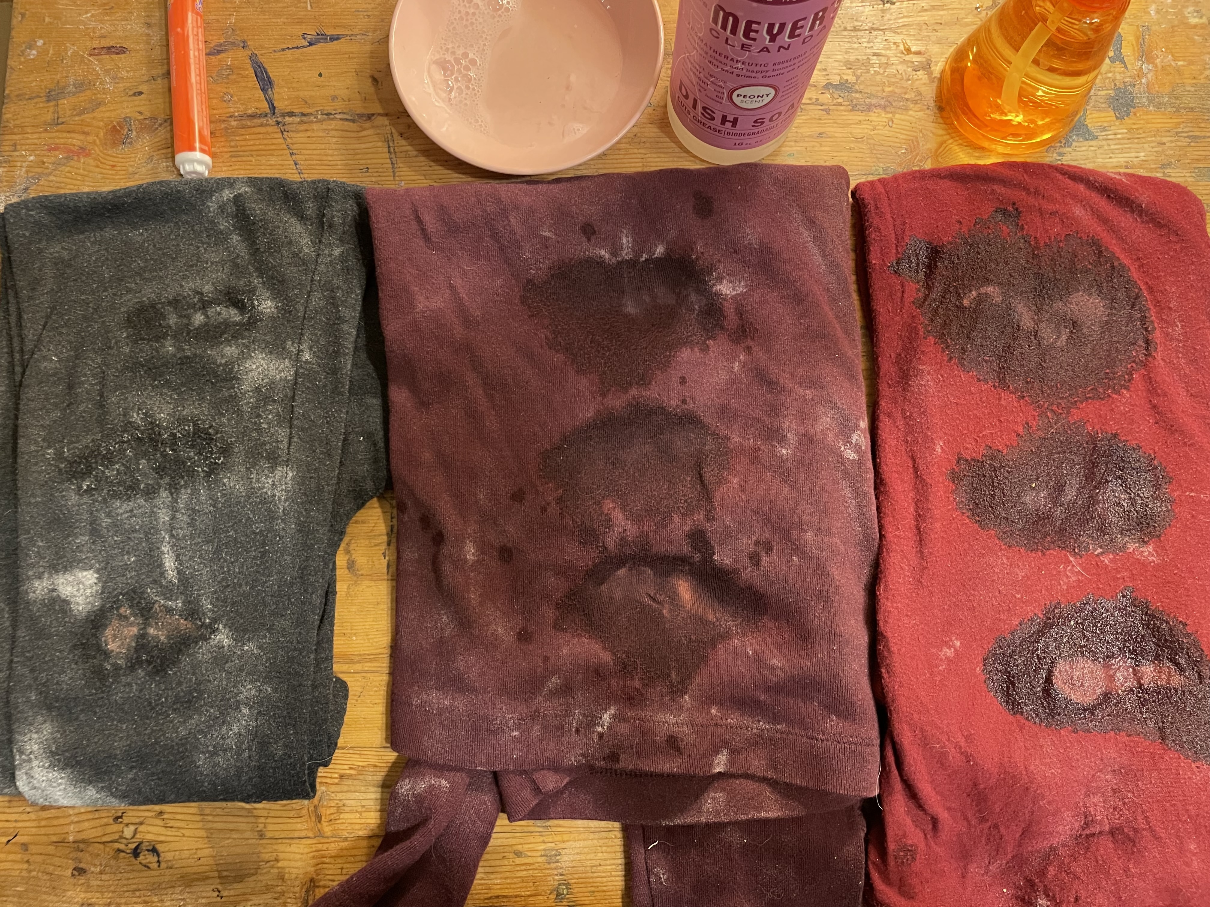 Three pieces of clothing with stains being pre-treated.