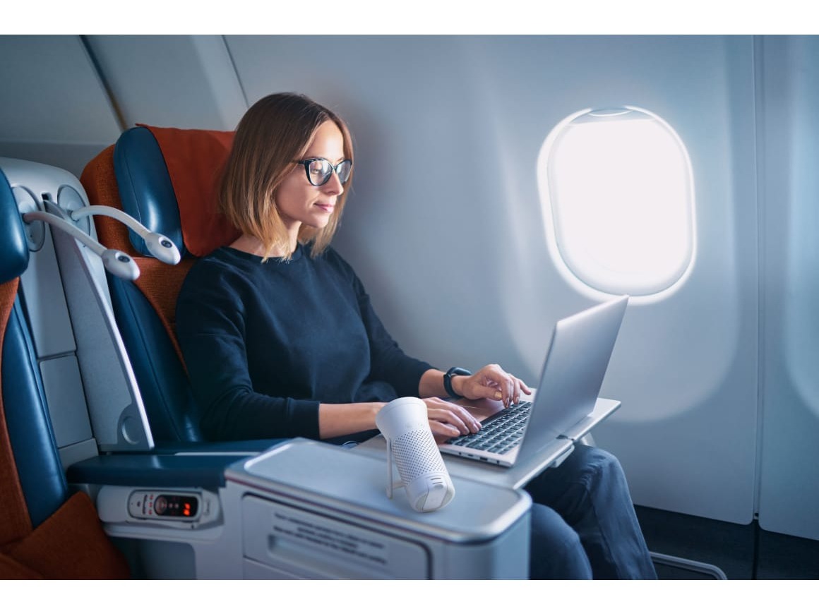 Image of a portable air purifier next to a person working on computer on an airplane