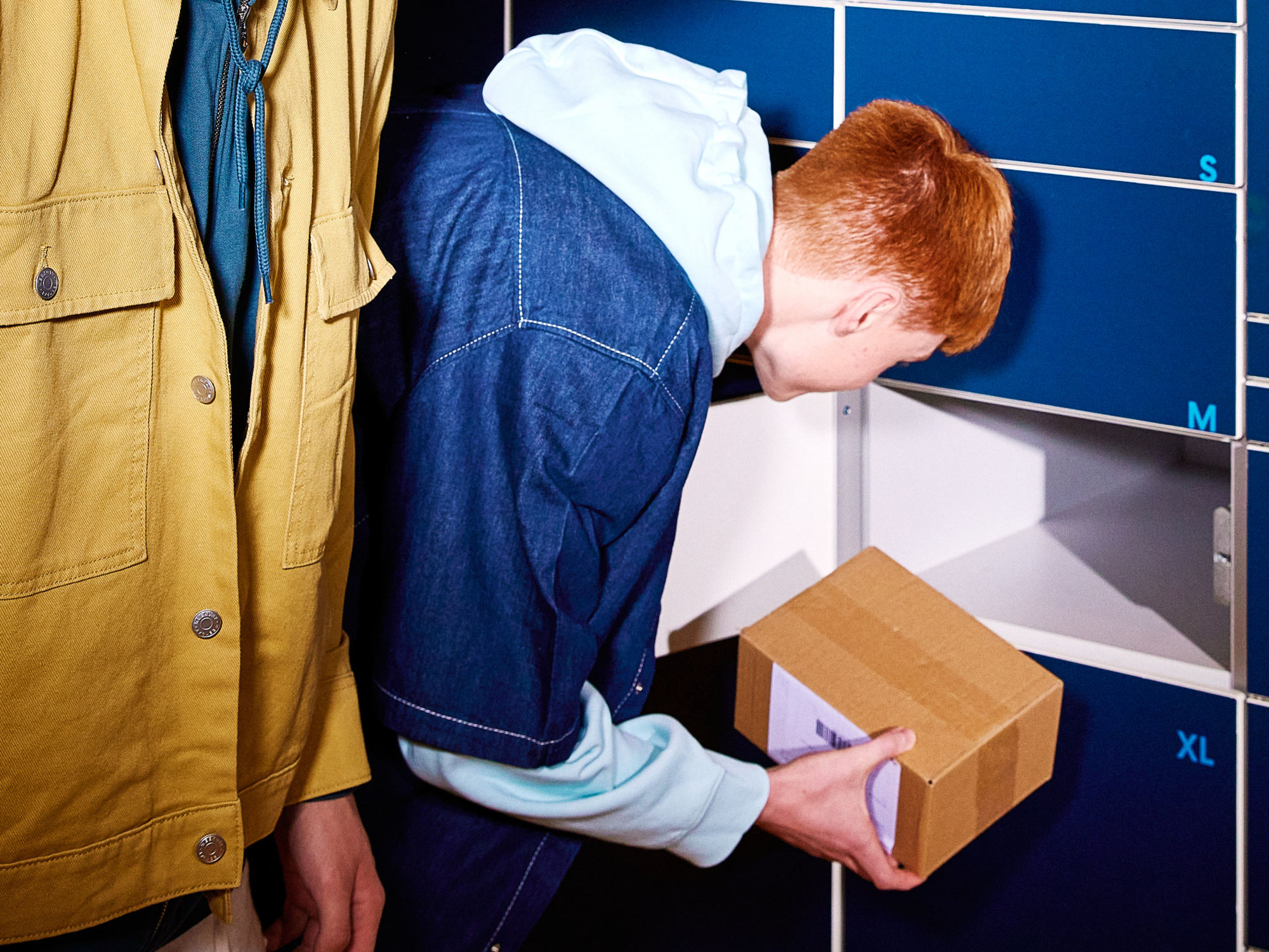 Nuori henkilö ottaa pakettia pakettiautomaatista, jossa on erikokoisia luukkuja.