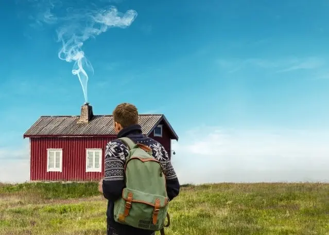 Mann på fjelltur foran rød hytte