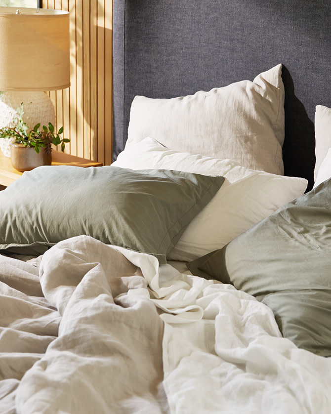 A bed with white, bone, and moss linen sheets
