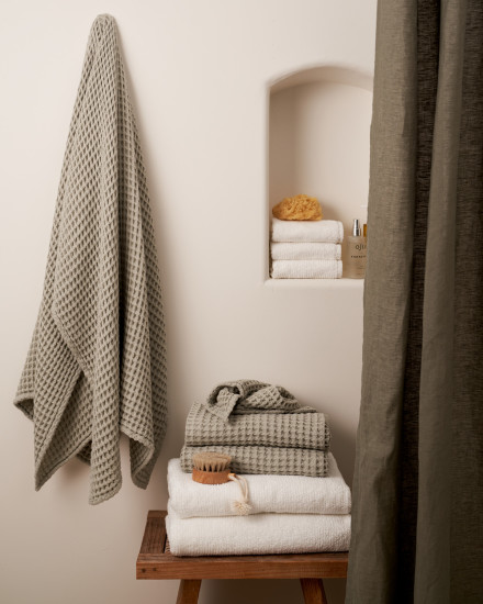 A willow green waffle towel hanging next to a stack of towels on a wooden bench