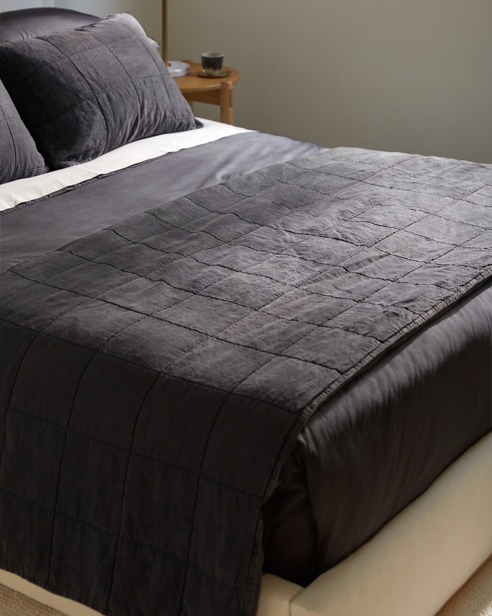 A dark grey coal linen quilt with a box pattern folded neatly at the foot of a bed