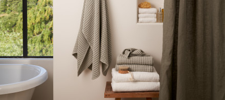 A bathroom with willow and white towels stacked neatly on a wooden stool