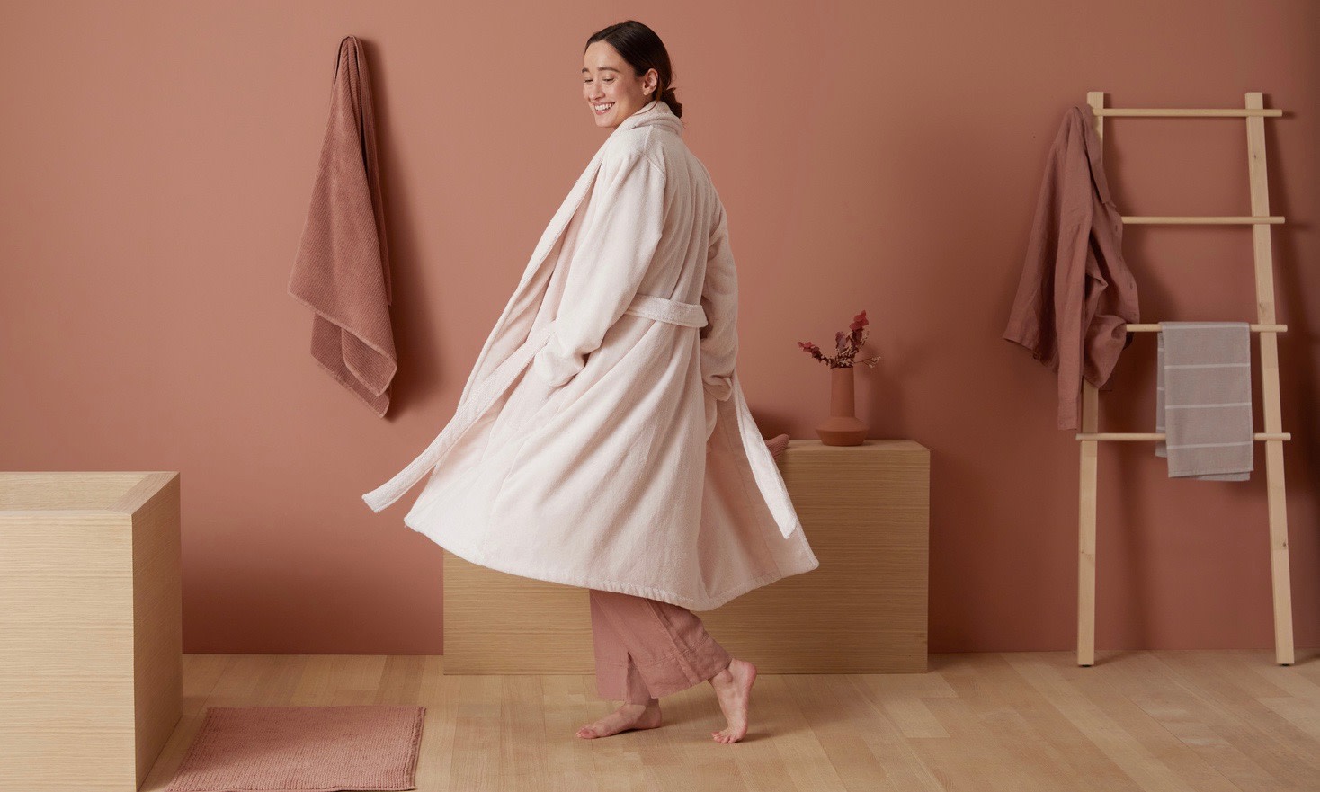 Woman in robe in clay colored bathroom. 