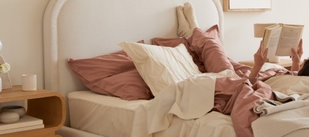 A person lounging in a bed with clay and ivory sheets