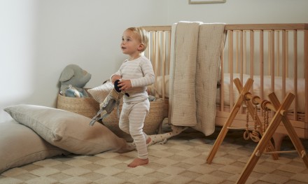 exceptionally cute toddler plays in a neutral nursery with an oversized elephant stuffy and a bone cloud cotton quilt
