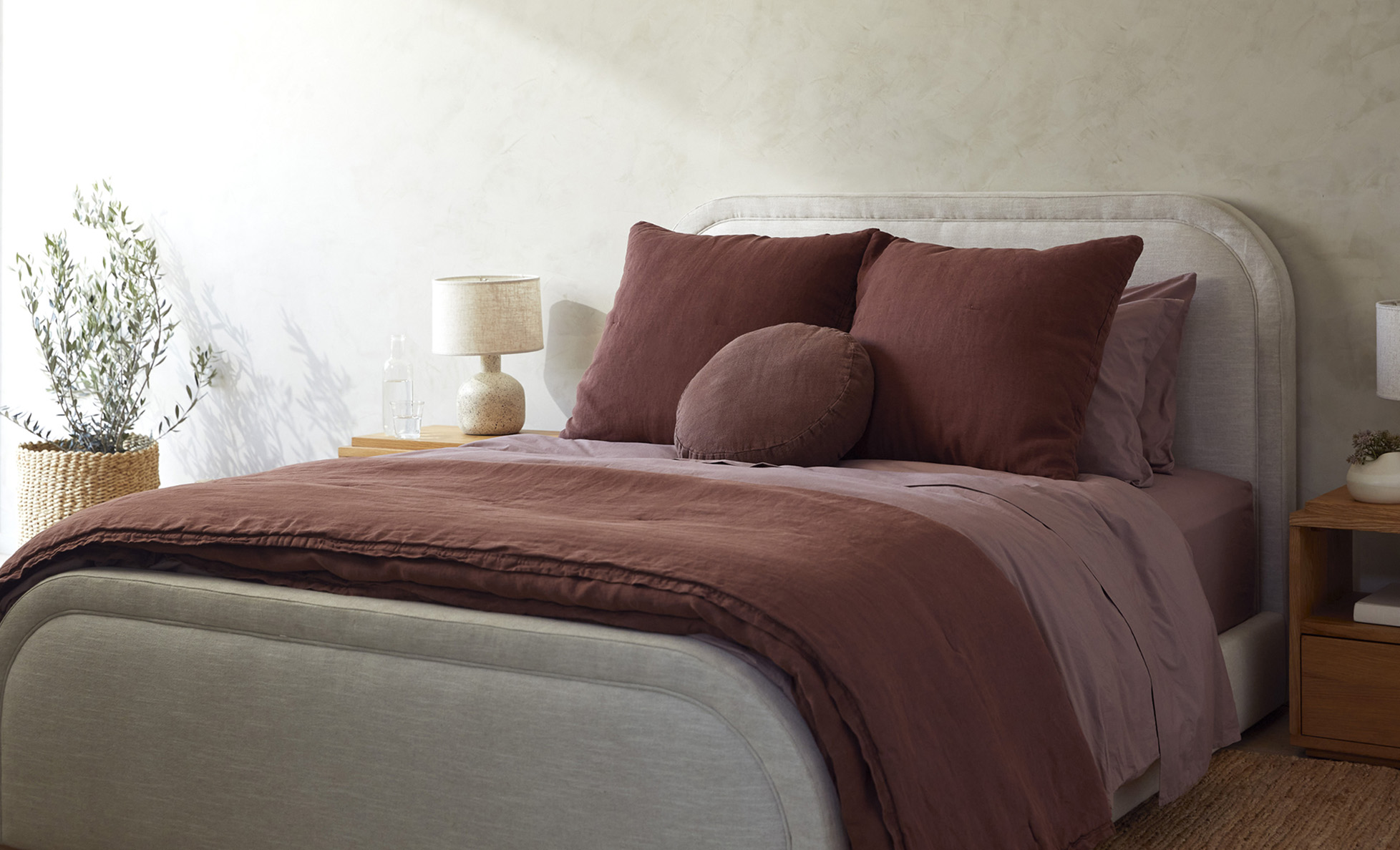 Neatly made bed with mauve purple sheets and raisin linen quilting