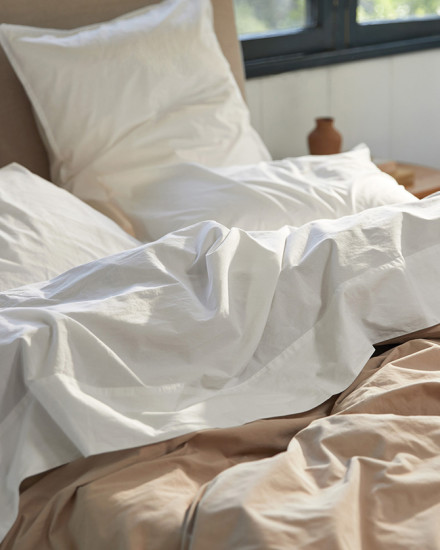 A messy bed with white and bisque organic cotton sheets