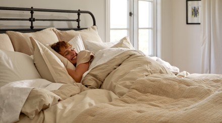 A person in a cozy bed with white and beige sheets and a cozy organic cloud cotton quilt