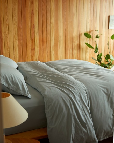 A bed with spa-blue cotton percale sheets in a wood-paneled room
