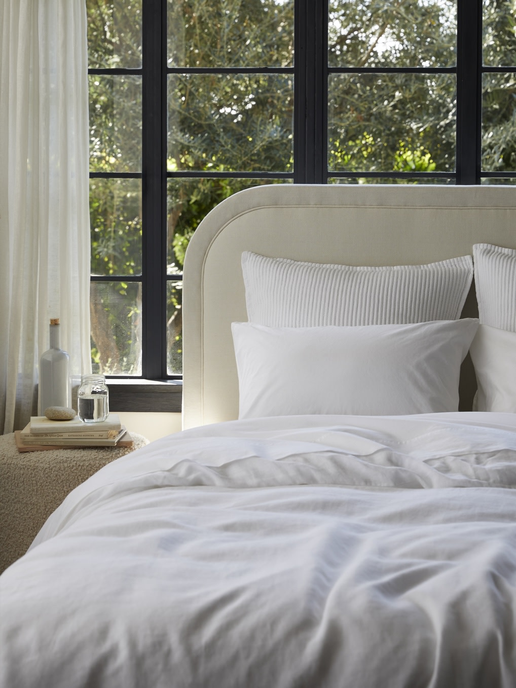 Linen and percale bedding on a cream headboard bed frame.