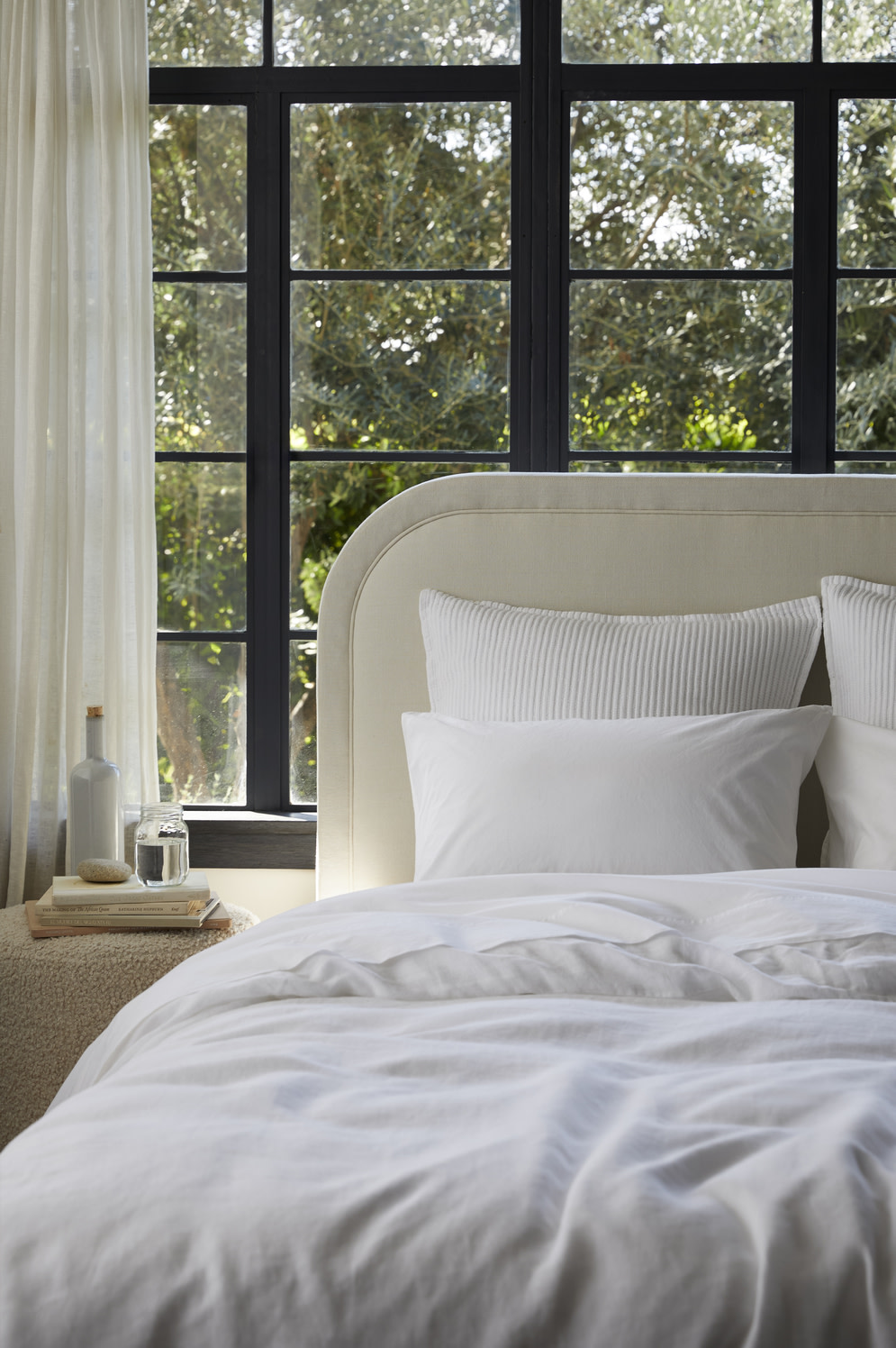 Linen and percale bedding on a cream headboard bed frame.