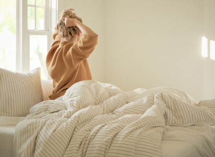 A woman sitting in a bed with Madewell x parachute sheets. 