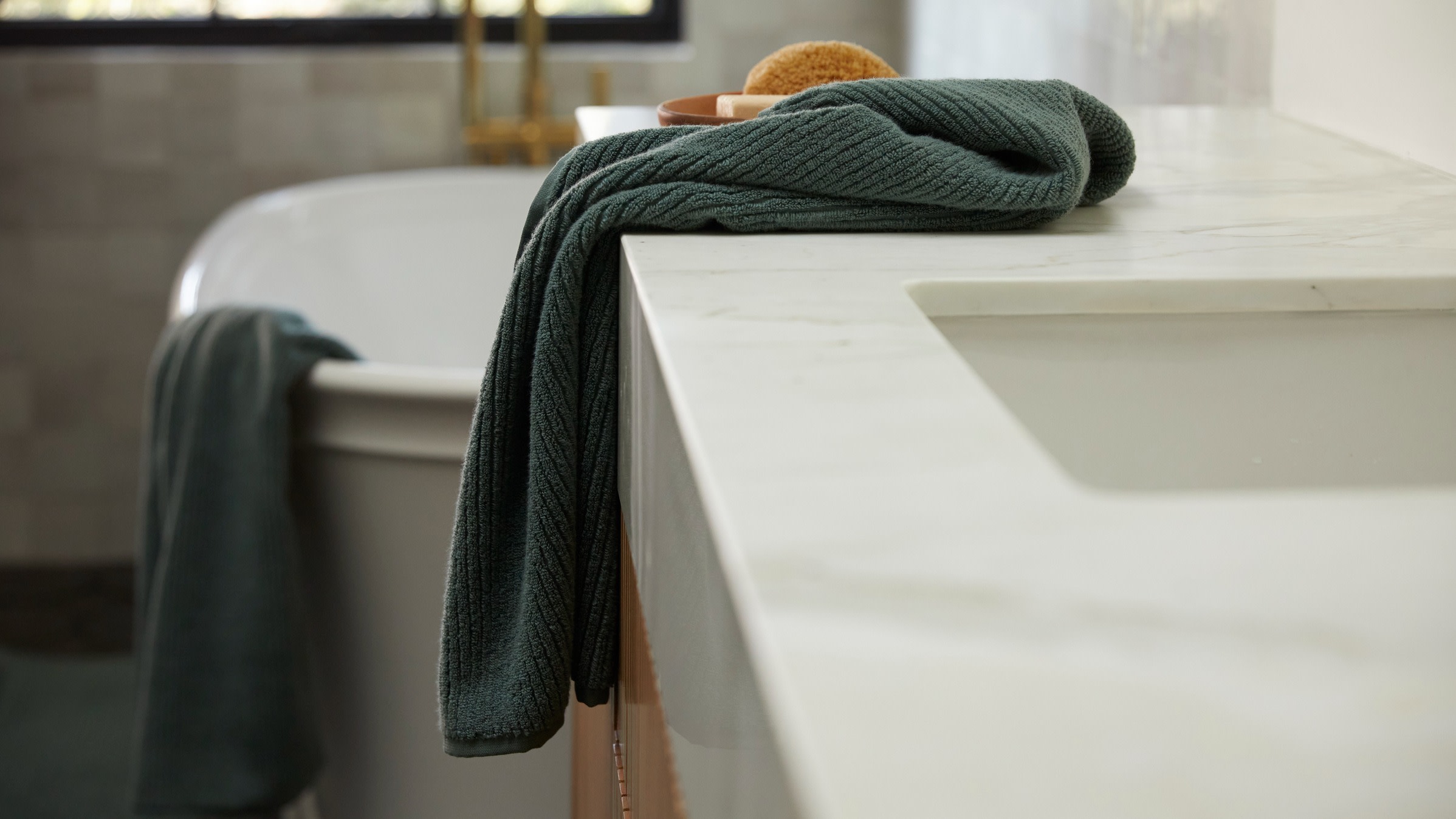An agave-green soft rib towel draped over the side of a marble bathroom counter