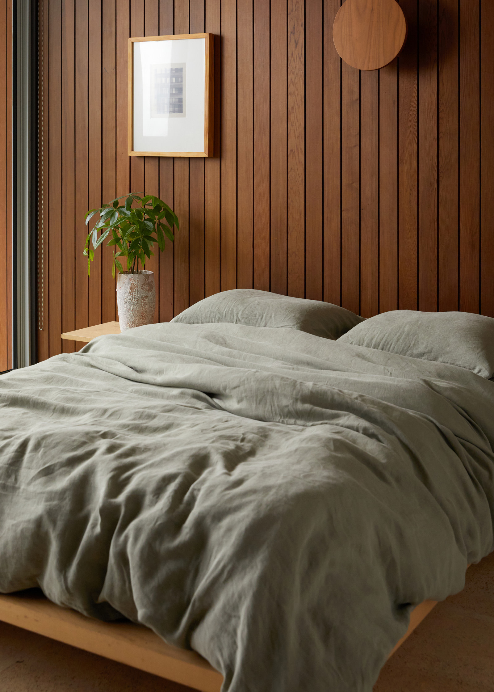 A bed with moss green linen sheets