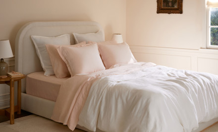 A neatly made bed with white and melon linen sheets