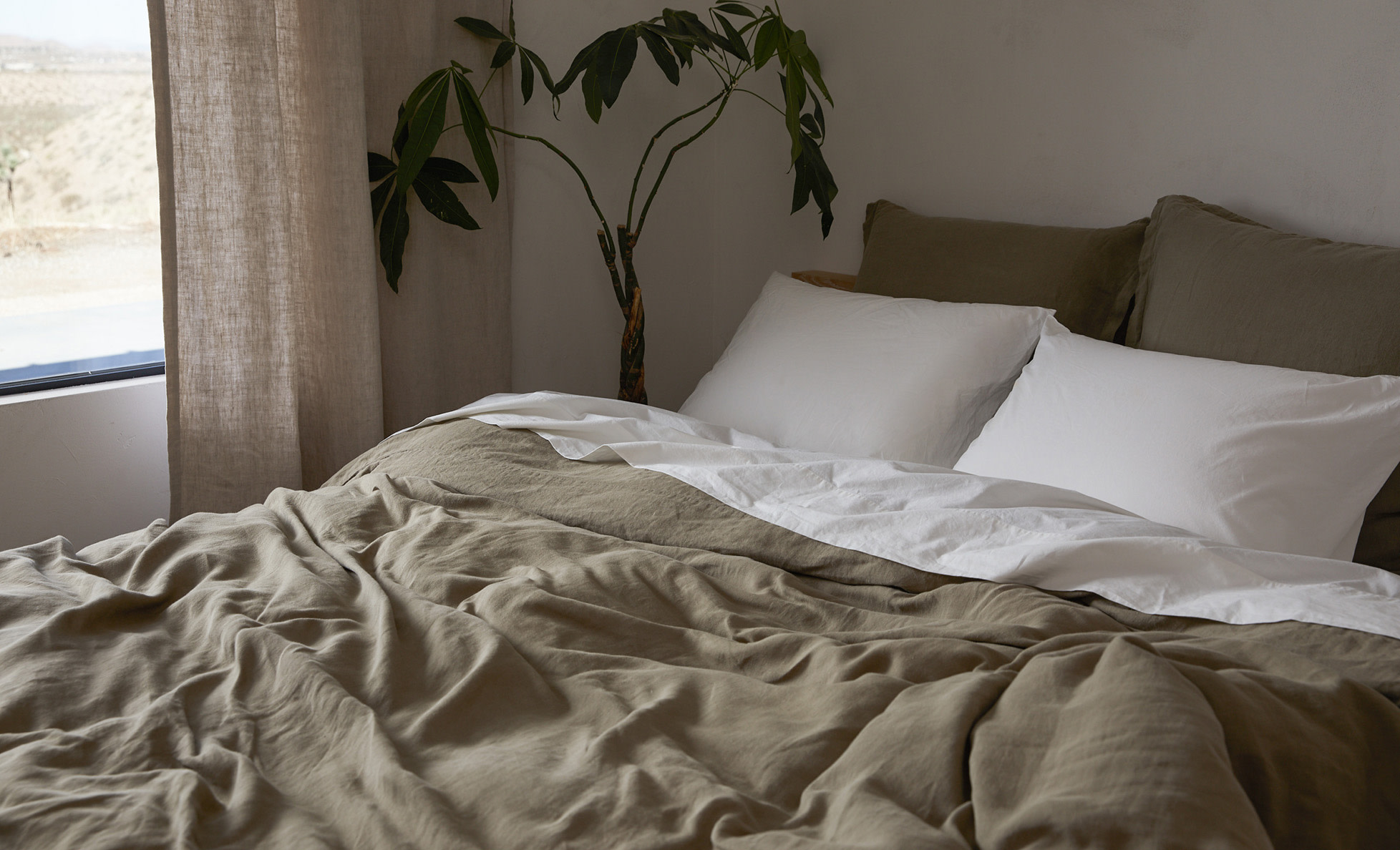 A bed with surplus green linen sheets
