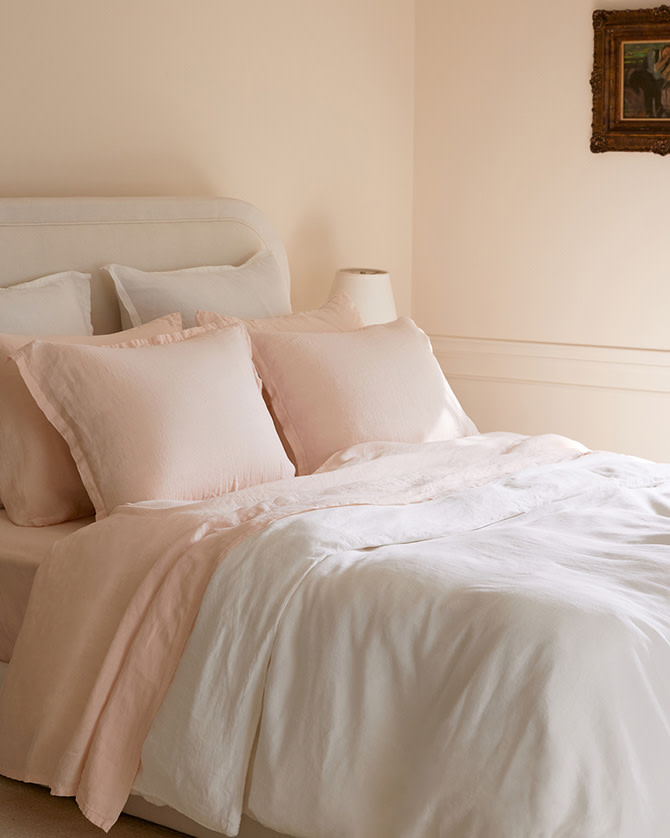A bed with white and melon linen sheets