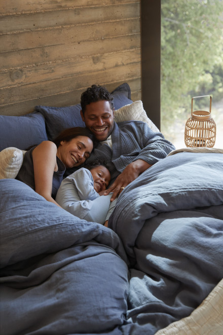 Dusk colored sheeting on a bed with a family cuddling