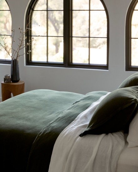 A bed with evergreen and white linen sheets