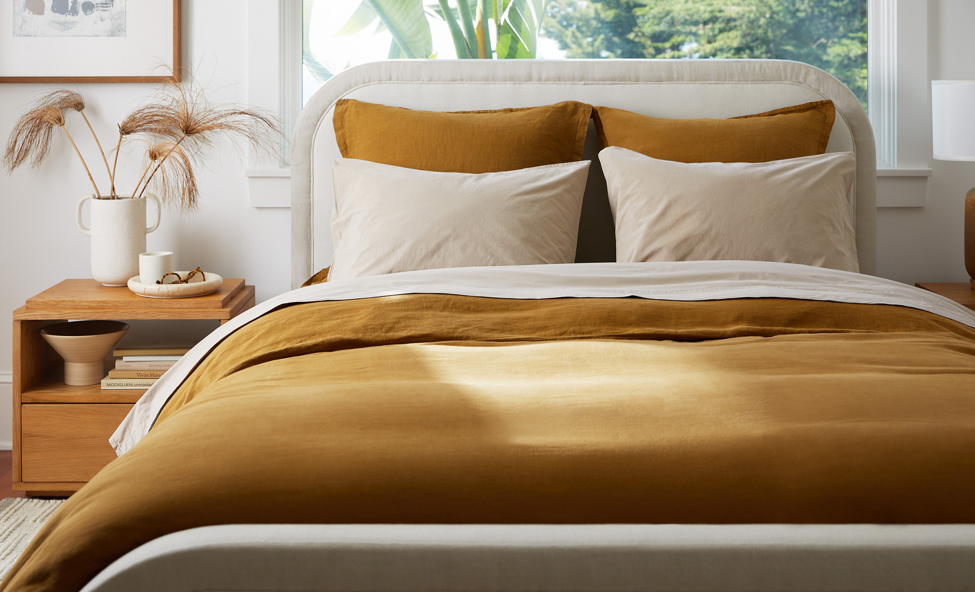 A neat bed with ochre linen and latte brushed cotton sheets