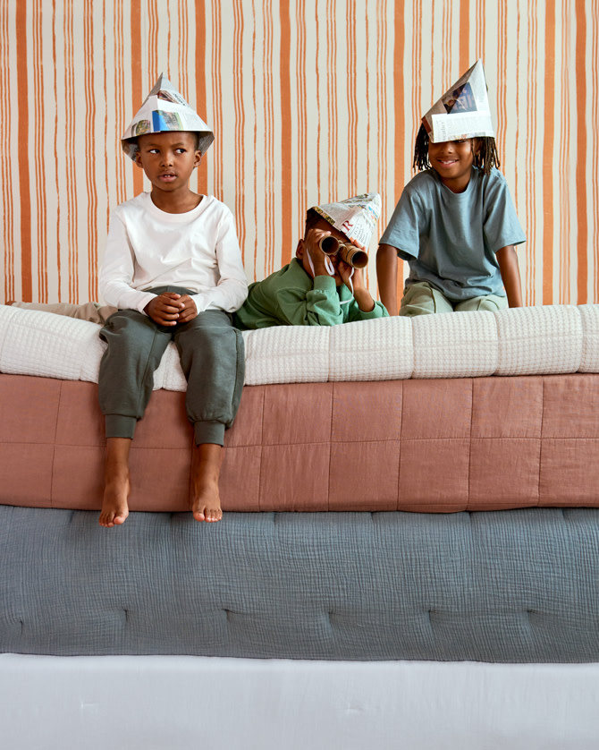 Three little boys sitting on top of stacked quilts, blankets, and mattresses