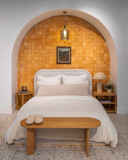 A neat bed made with cream and white linen sheets under an archway