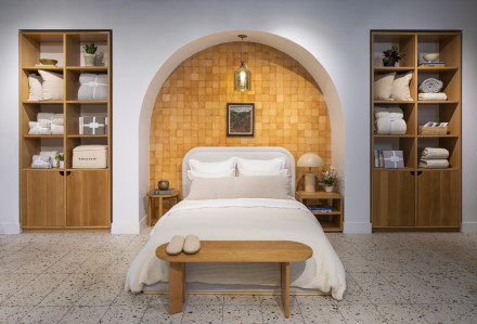 A neat bed made with cream and white linen sheets under an archway