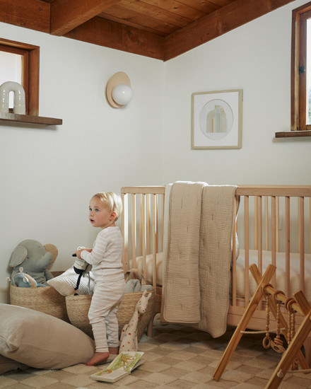 A baby in a brightly lit nursery with a checkered wool rug