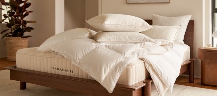 A bare Parachute mattress on a dark walnut wood bed frame with pillow and duvet inserts tossed on top
