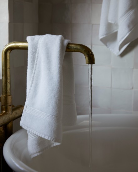 A white towel hanging over a brass bath tub faucet