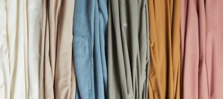 A gradient of cotton sheets in warm tones of ivory, blue, green, yellow, and pink