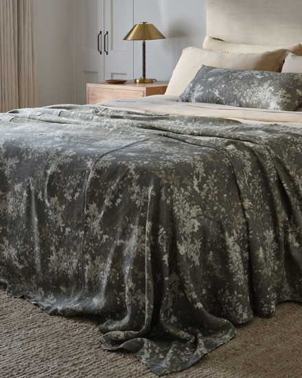 A sage botanical print bedspread softly layered on a stylish bed