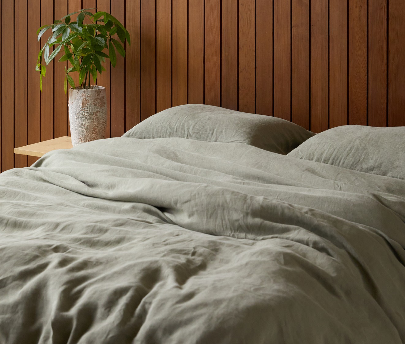 A simple bed with moss green linen sheets