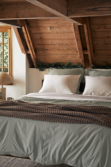 A neat bed with white and moss percale sheets and a soft brown throw blanket