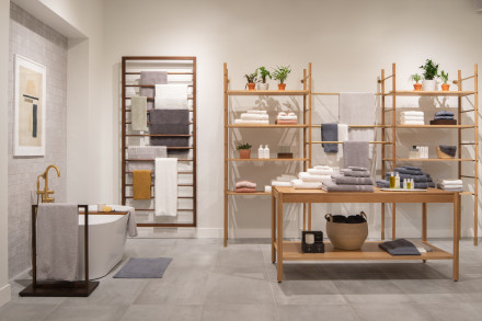 Bath towels folded and hung neatly on light wooden shelving alongside a freestanding bathtub.