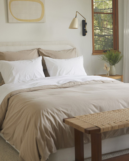 A neat bed with white and bisque organic cotton sheets