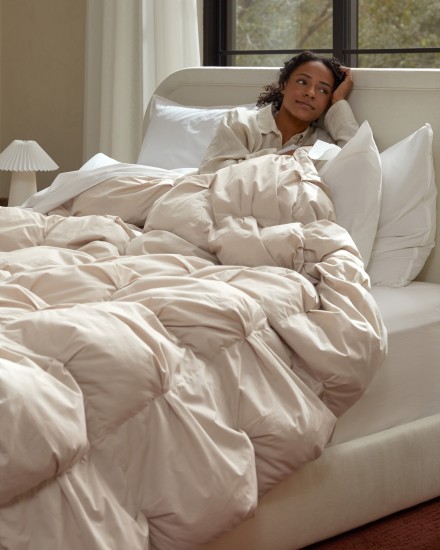 A woman sitting in a cozy bed with a plush puffy pintucked comforter
