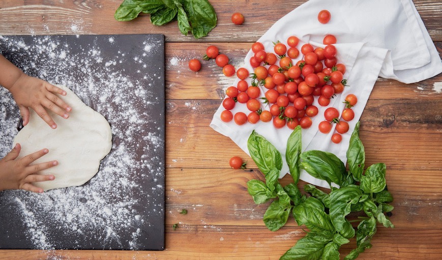 Toddler hands with dough, tomatoes and basil 