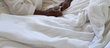 A person lounging in a bed of crisp white cotton sheets and a cozy white Organic Cloud Cotton Quilt