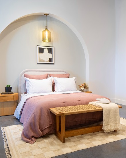 Neatly made bed with clay bedding next to shelves filled with various blankets and sheets