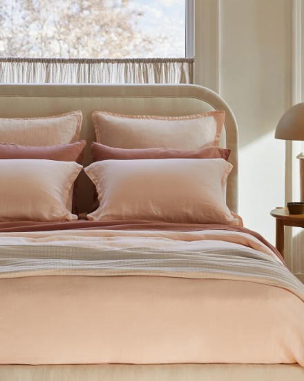 A bed with melon and clay pink linen sheets