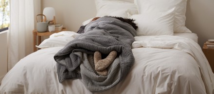 A person wrapped in a cozy grey quilt with their feet sticking out