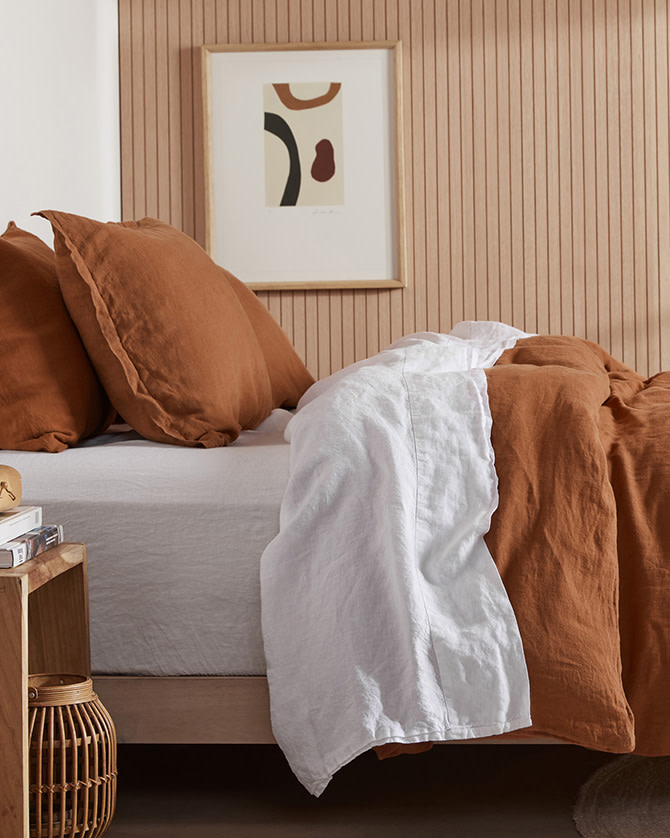 A bed with white and terra linen sheets