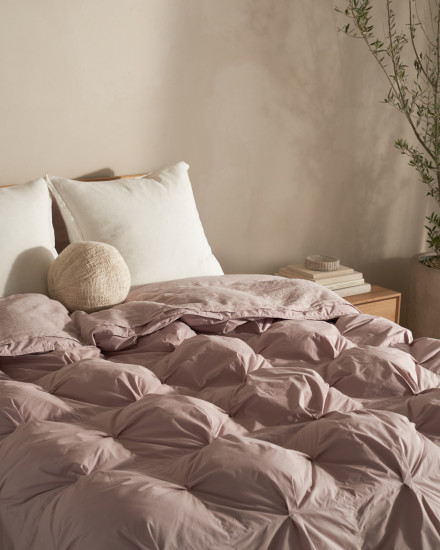 A bed with a haze-colored organic cotton puff comforter and a sphere boucle pillow