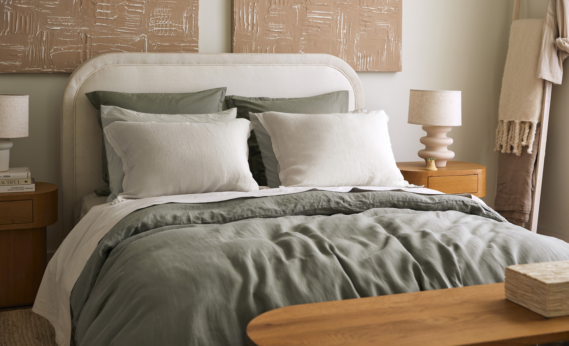 Neatly made bed with light green and taupe linen sheets